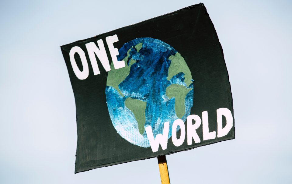 A black sign with the earth and the words "one world" on it at a climate rally. Protestors encourage corporations to make their businesses more sustainable.